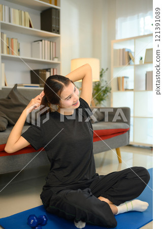 Cheerful asian young woman stretching on a yoga mat in her living room 121391089