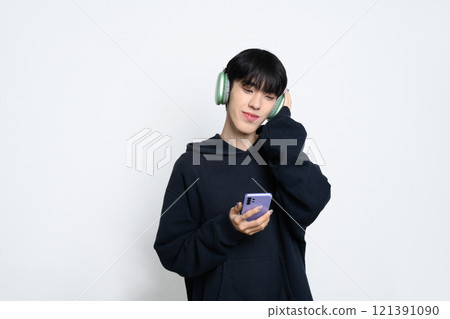 Relaxed teenage man listening to music with headphones using mobile phone on white background Relaxed teenage man listening to music with headphones using mobile phone on white background 121391090