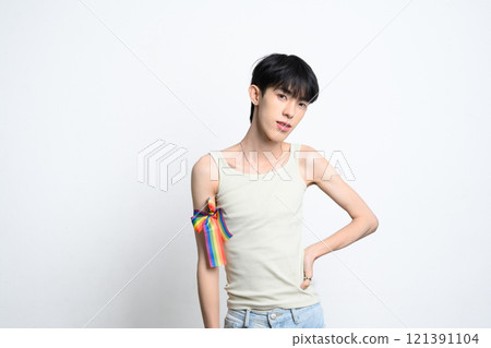 Cute man with rainbow ribbon tied on their arm posing confidently on white background. LGBTQ pride and equality concept Cute man with rainbow ribbon tied on their arm posing confidently on white background. LGBTQ pride and equality concept 121391104