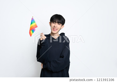 Confident young man wearing dark hoodie holding a small rainbow pride flag, celebrating LGBTQ pride 121391106