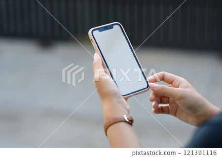 Close up of young woman using her smartphone while walking on the street outdoors Close up of young woman using her smartphone while walking on the street outdoors 121391116