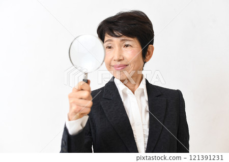 Asian middle-aged woman in a suit holding a magnifying glass Asian middle-aged woman in a suit holding a magnifying glass 121391231