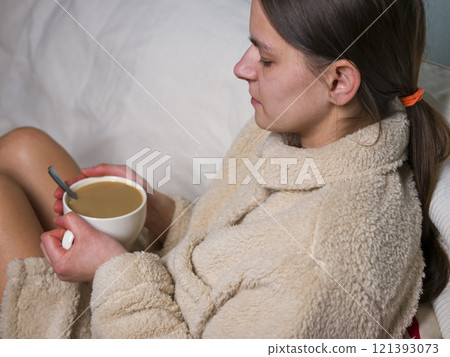 Relaxed young woman in comfortable bathrobe enjoying cozy moment with warm cup of coffee and on the sofa Relaxed young woman in comfortable bathrobe enjoying cozy moment with warm cup of coffee and on the sofa 121393073
