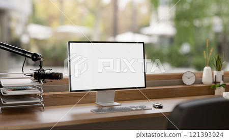 A minimalist podcast studio featuring a microphone, a computer with a white screen mockup, and decor A minimalist podcast studio featuring a microphone, a computer with a white screen mockup, and decor 121393924