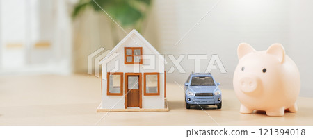 Piggy bank with house and blue car models symbolizes saving money for a dream home and auto. Highlights property investment, asset building, and expense management with finance Piggy bank with house and blue car models symbolizes saving money for a dream home and auto. Highlights property investment, asset building, and expense management with finance 121394018