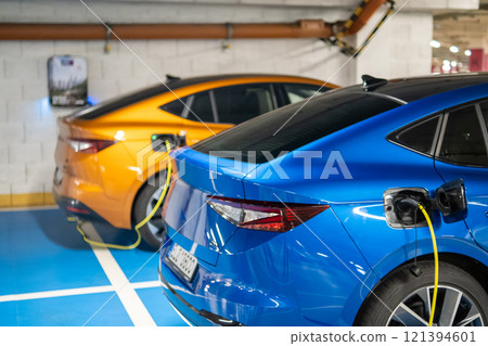 Electric vehicles blue and orange charging in a modern parking garage  121394601