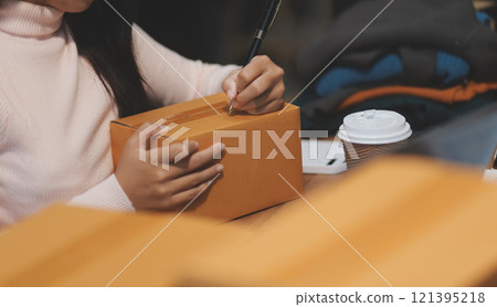 Startup SME small business entrepreneur of freelance Asian woman wearing apron using laptop and box to receive and review orders online to prepare to pack sell to customers, online sme business ideas. Startup SME small business entrepreneur of freelance Asian woman wearing apron using laptop and box to receive and review orders online to prepare to pack sell to customers, online sme business ideas. 121395218