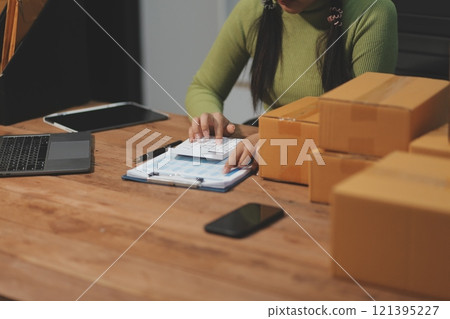 Startup SME small business entrepreneur of freelance Asian woman wearing apron using laptop and box to receive and review orders online to prepare to pack sell to customers, online sme business ideas. 121395227