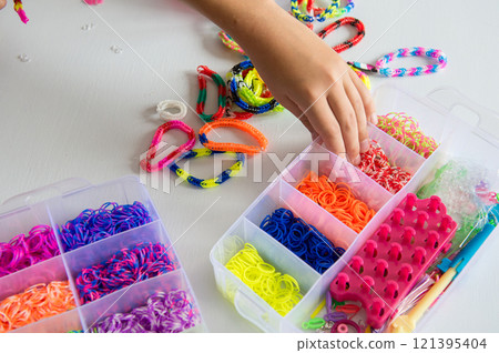 Hand picking colorful rubber bands from storage box on white table. 121395404
