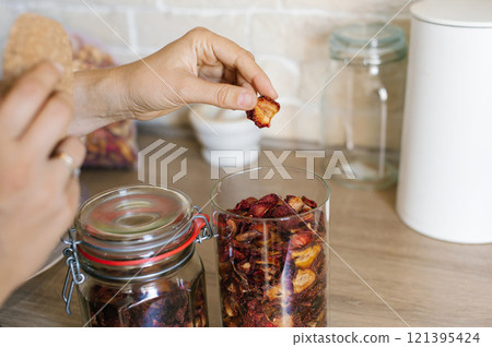 Woman Organizes Dried Fruit in Glass Jars on Kitchen Countertop Woman Organizes Dried Fruit in Glass Jars on Kitchen Countertop 121395424