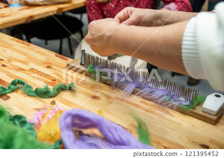 Caucasian female adult preparing wool fibers for weaving on wooden carding board Caucasian female adult preparing wool fibers for weaving on wooden carding board 121395452