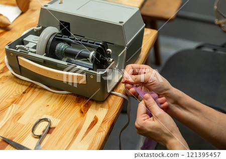 Distaff Day Hands threading a vintage sewing machine for needlework on a wooden table 121395457