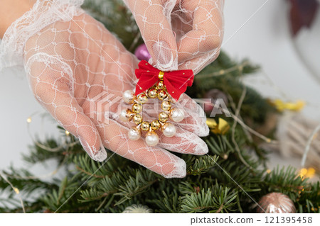 Female hand decorates christmas tree with festive ornament and red bow 121395458