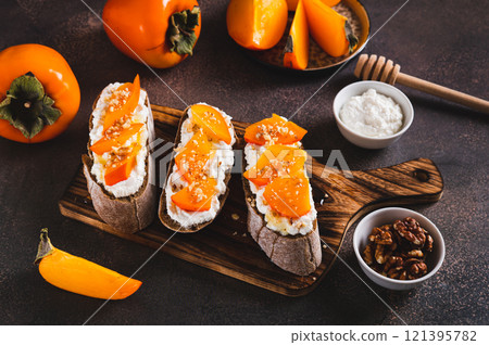 Sweet bruschetta with persimmon and ricotta on a board on a table 121395782