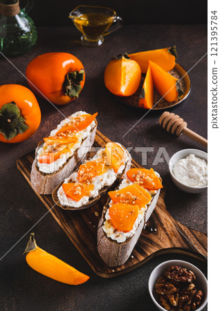 Sweet bruschetta with persimmon and ricotta on a board on a table vertical view 121395784