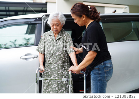 Caregiver help Asian elderly woman disability patient get in her car. 121395852