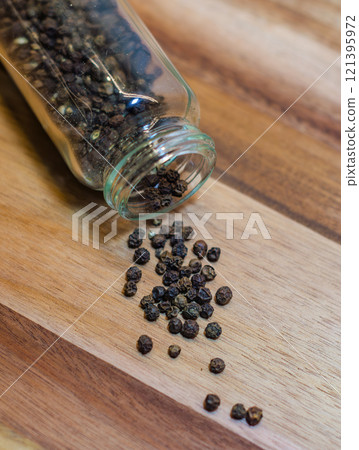 Black Peppercorns Spilled from a Glass Jar on wooden background. High quality photo 121395972