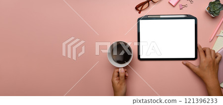 Overhead view of hand holding cup of coffee and using digital tablet on pink pastel background with copy space 121396233