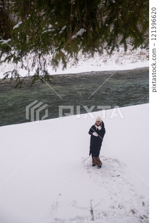 Person on Snowy Riverbank with Forest and Bridge Person on Snowy Riverbank with Forest and Bridge 121396620