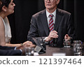 Cropped shot of senior politician in suit answering questions chairing committee while sitting at table with other administration officials during press conference, copy space 121397464