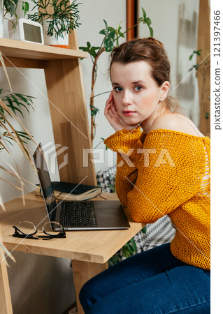 happy young woman is sitting at desk in home office, looking at laptop screen studying 121397466