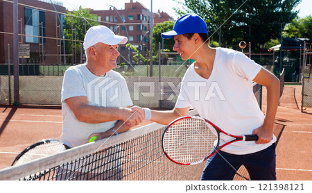 Mature senior and young man shake hands before tennis match 121398121