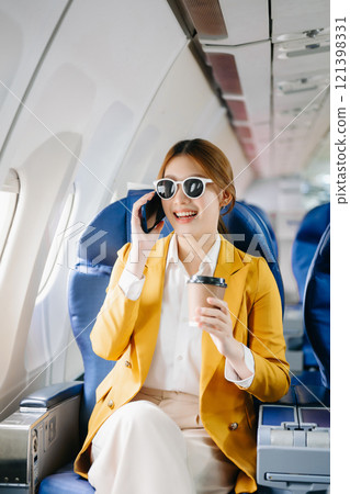 Attractive Asian female passenger of airplane sitting in comfortable seat while working laptop and tablet 121398331