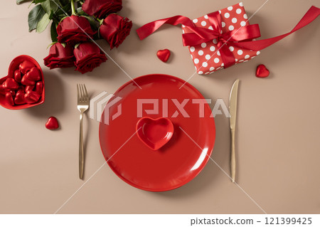 Valentine's day. Romantic dinner for date with red plate, chocolate sweets, romantic gift and red roses on beige background. View from above. Copy space. Valentine's day. Romantic dinner for date with red plate, chocolate sweets, romantic gift and red roses on beige background. View from above. Copy space. 121399425