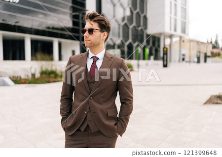 Portrait of successful businessman in stylish suit walking in downtown, exuding success and professionalism. Determined ambitious business man in sunglasses embodying modern leadership outside. 121399648