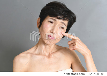 A middle-aged Asian woman with a troubled face pointing at her eyes 121400186