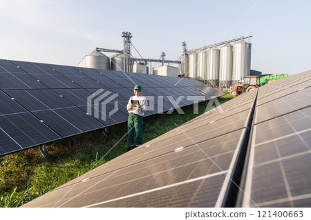 Female farmer with digital tablet on a modern farm using solar panels. Agricultural silos in the background Female farmer with digital tablet on a modern farm using solar panels. Agricultural silos in the background 121400663