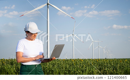 Woman farmer wearing white cap and t-shirt with laptop. Wind turbines in the background. Woman farmer wearing white cap and t-shirt with laptop. Wind turbines in the background. 121400665
