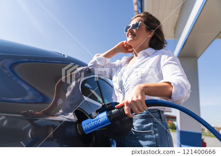 Woman holds a hydrogen fueling nozzle on a hydrogen filling station. Refueling car with hydrogen fuel. Woman holds a hydrogen fueling nozzle on a hydrogen filling station. Refueling car with hydrogen fuel. 121400666