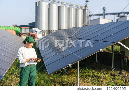 Female farmer with digital tablet on a modern farm using solar panels. Agricultural silos in the background. Female farmer with digital tablet on a modern farm using solar panels. Agricultural silos in the background. 121400695