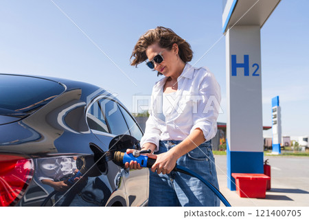 Woman holds a hydrogen fueling nozzle on a hydrogen filling station. Refueling car with hydrogen fuel 121400705