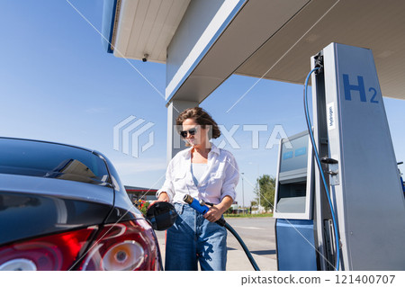 Woman holds a hydrogen fueling nozzle on a hydrogen filling station. Refueling car with hydrogen fuel Woman holds a hydrogen fueling nozzle on a hydrogen filling station. Refueling car with hydrogen fuel 121400707
