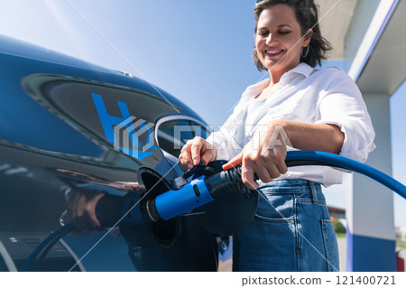 Woman holds a hydrogen fueling nozzle on a hydrogen filling station. Refueling car with hydrogen fuel 121400721