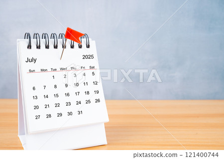 July 2025 calendar and red push pin on table. 121400744