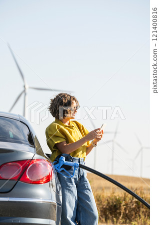 Woman with fueling hydrogen car. Refueling car with hydrogen fuel. Wind turbines in the background Woman with fueling hydrogen car. Refueling car with hydrogen fuel. Wind turbines in the background 121400816