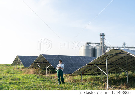 Female farmer with digital tablet on a modern farm using solar panels. Agricultural silos in the background Female farmer with digital tablet on a modern farm using solar panels. Agricultural silos in the background 121400833