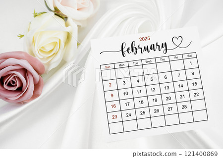 February 2025 calendar page and rose flower on white satin textile. 121400869