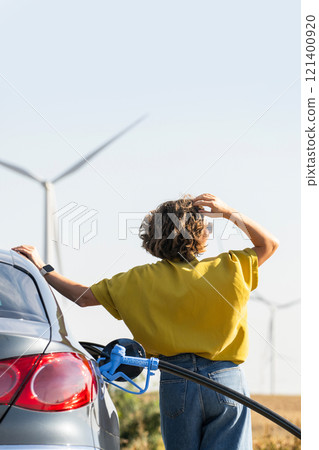 Woman with fueling hydrogen car. Refueling car with hydrogen fuel. Wind turbines in the background. 121400920