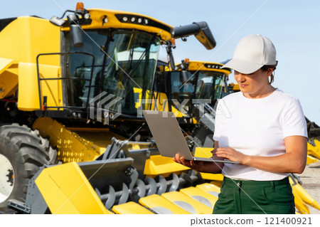 Female farmer with laptop on a background of harvester. Smart farming concept. Female farmer with laptop on a background of harvester. Smart farming concept. 121400921