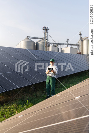 Female farmer with digital tablet on a modern farm using solar panels. Agricultural silos in the background 121400922