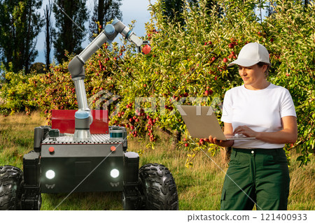 Farmer controls autonomous robot harvester with robotic arm harvesting apples on a smart farm. Concept. Farmer controls autonomous robot harvester with robotic arm harvesting apples on a smart farm. Concept. 121400933