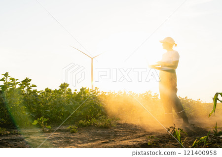 Woman farmer wearing white cap and t-shirt with laptop. Wind turbines in the background Woman farmer wearing white cap and t-shirt with laptop. Wind turbines in the background 121400958