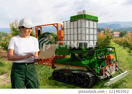 Farmer controls autonomous robot sprayer in a fruit garden. Smart farming concept. 121401052