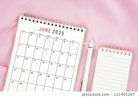 June 2025 month calendar and pen with open diary on pink fabric background. 121401267