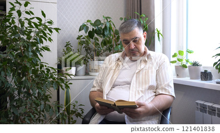 Man Reading Book in Armchair Surrounded by Indoor Plants 121401838