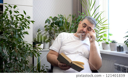 A man in a cozy chair read a book and fell asleep A man in a cozy chair read a book and fell asleep 121401839